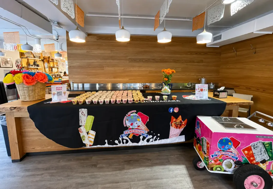 A La Michoacana Premium catering table lined with prepared cups next to a branded paleta cart at an indoor event.