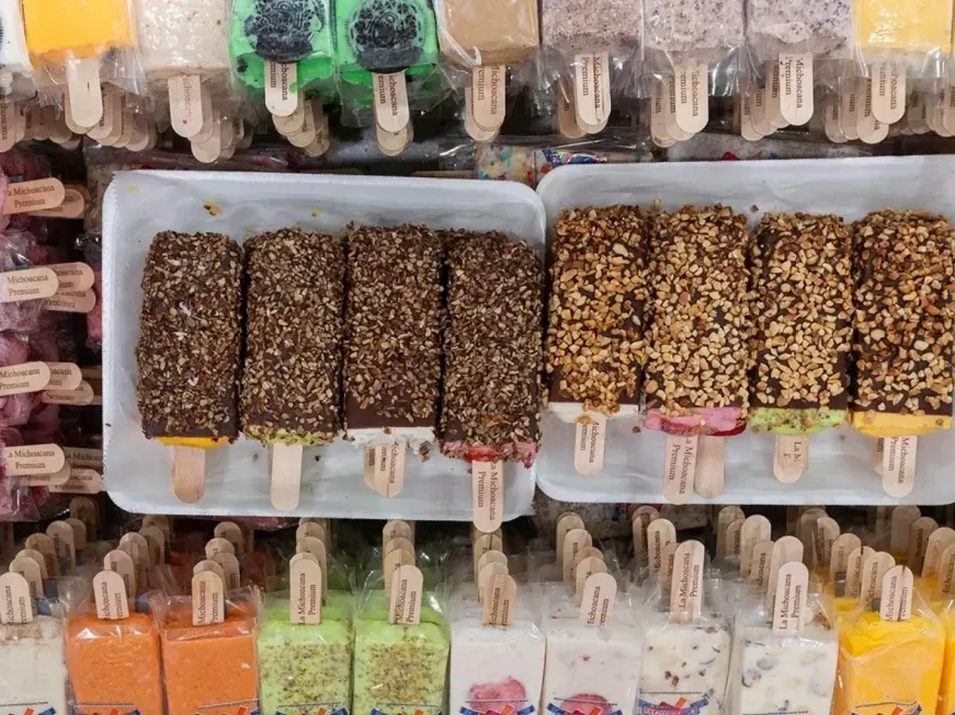 Rows of wrapped La Michoacana Premium paletas in the case, with trays of chocolate-dipped bars coated in nuts and coconut.