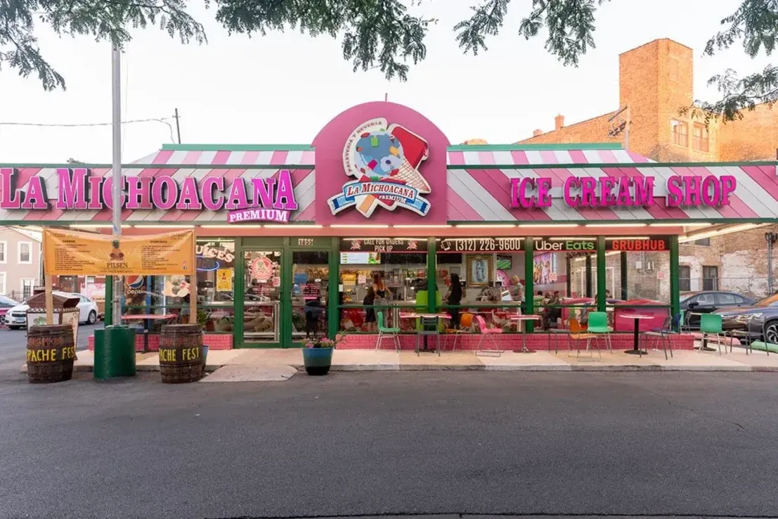 The pink exterior of La Michoacana Premium Pilsen on South Blue Island Avenue, with its striped awning, ice cream shop signage, and sidewalk seating.